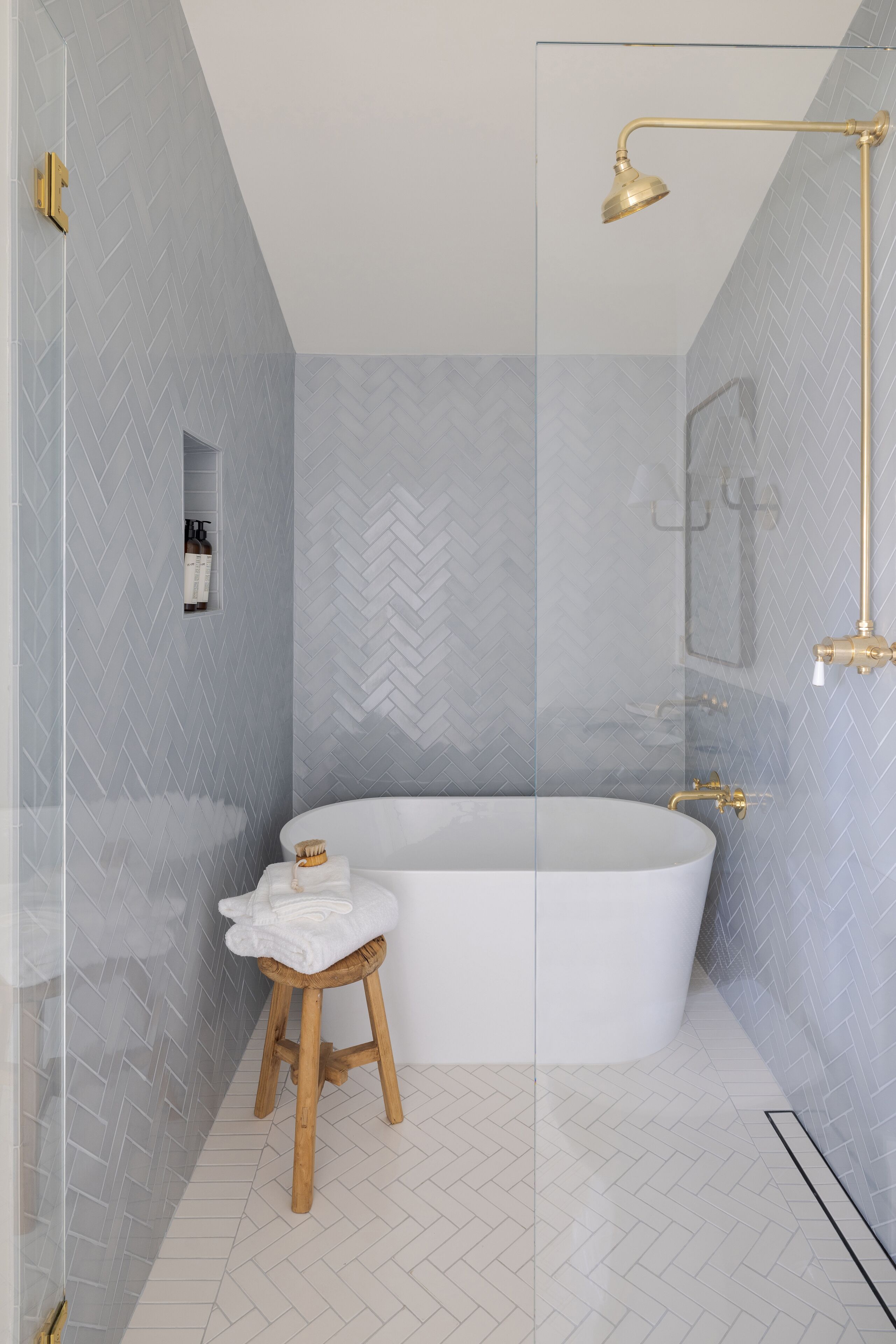 Un baño moderno con una bañera independiente, cabina de ducha con mampara de vidrio y un taburete de madera con una toalla.