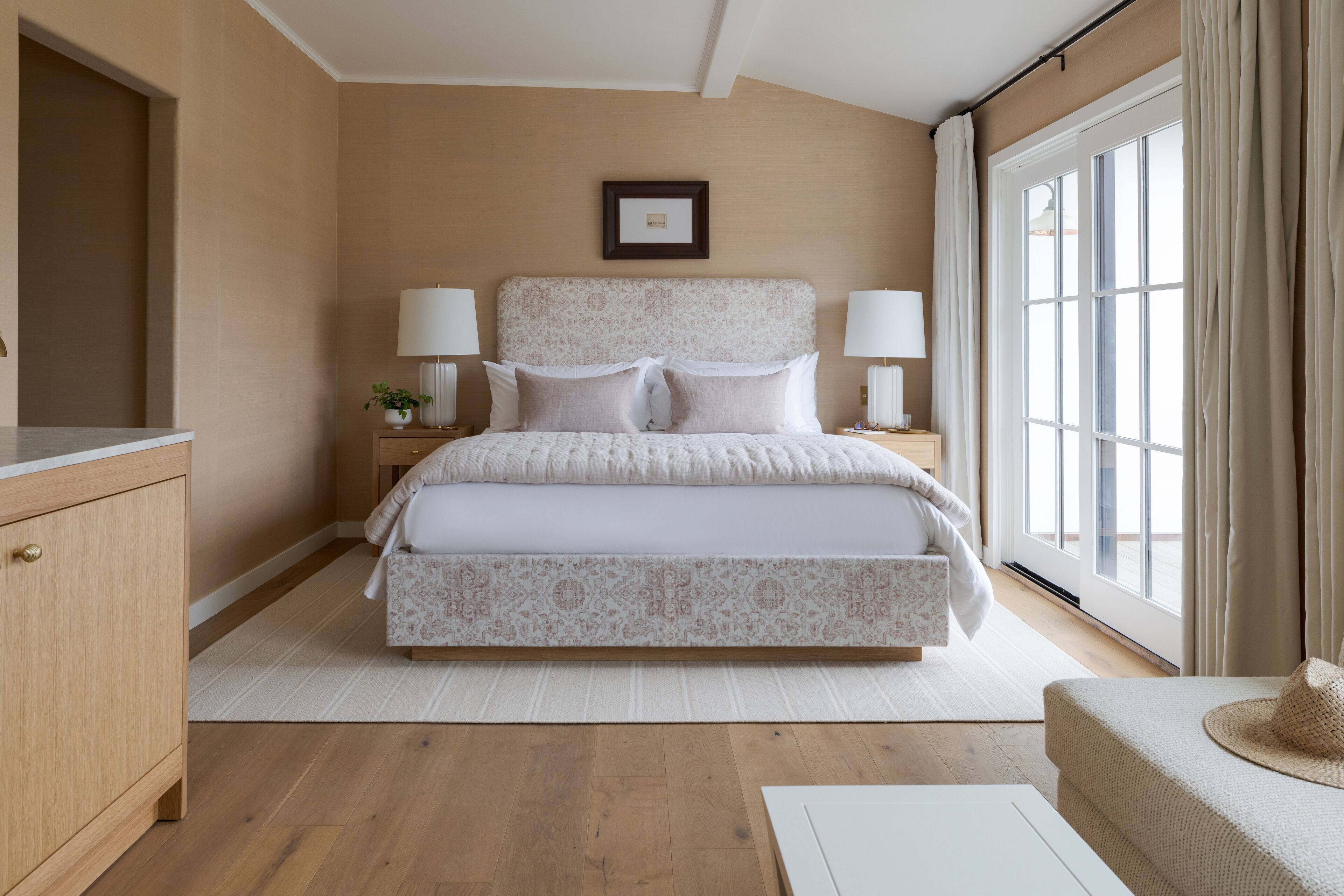 Une chambre à coucher avec un grand lit, des lampes de chevet, une table de chevet, une commode en bois et une grande fenêtre avec des rideaux.