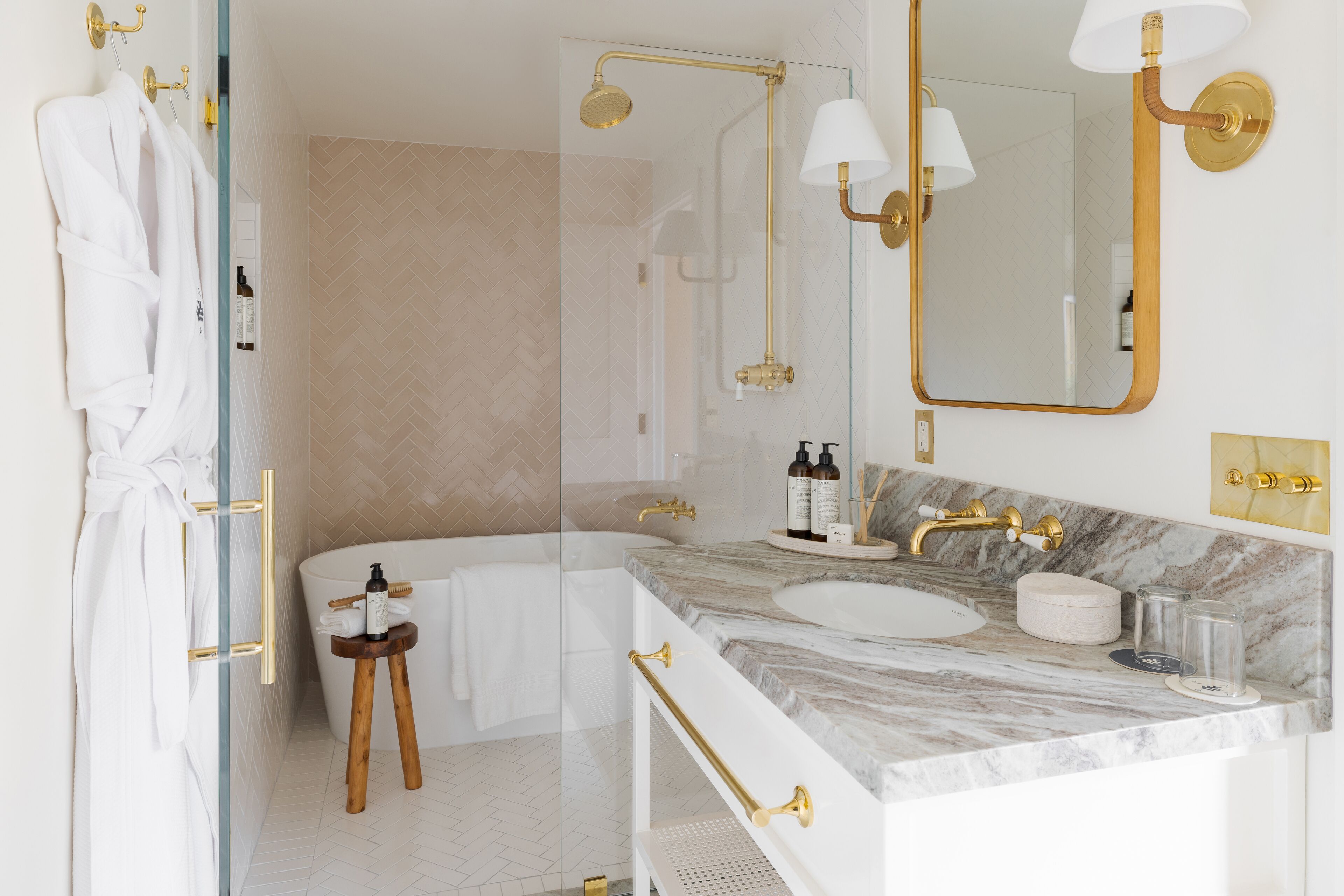 A modern bathroom with a freestanding bathtub, a marble vanity, gold fixtures, and a glass shower enclosure.