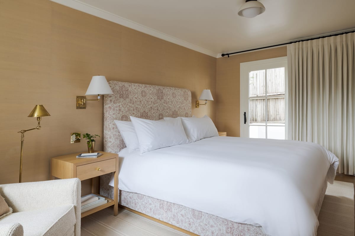 A neatly arranged bedroom with a large bed, bedside lamps, a nightstand, and a chair.