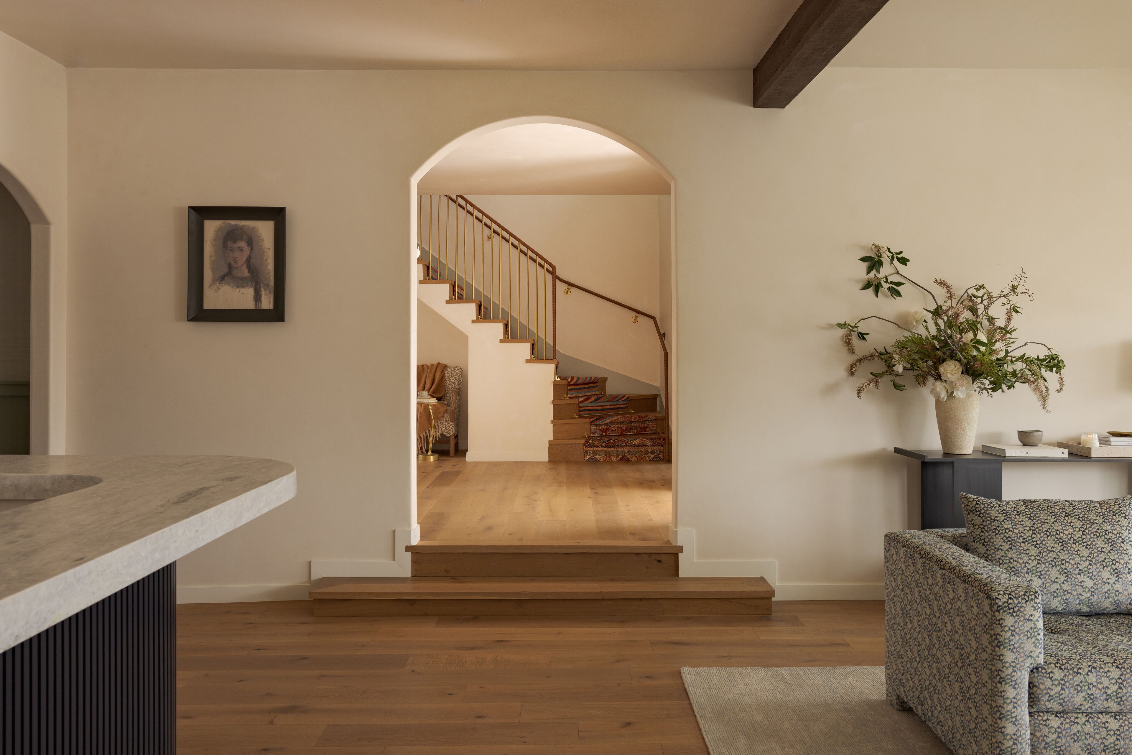A modern interior with a wooden staircase, a cushioned seating area, and a vase with flowers.