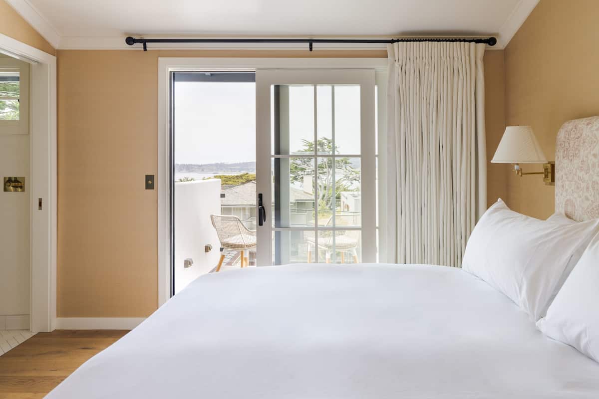 A hotel room with a large bed, a balcony with a chair, and a view of the city.