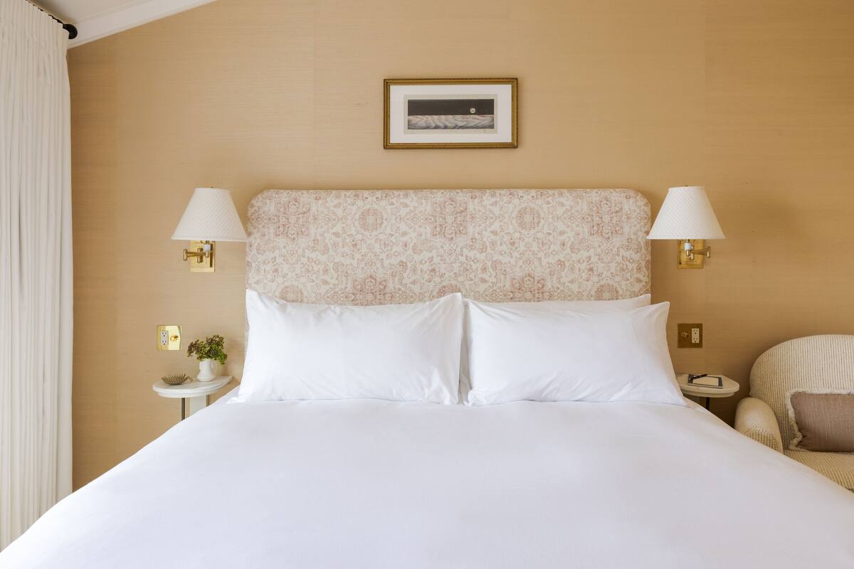 A hotel room with a large bed, two bedside lamps, a small table with a plant, and a framed picture on the wall.