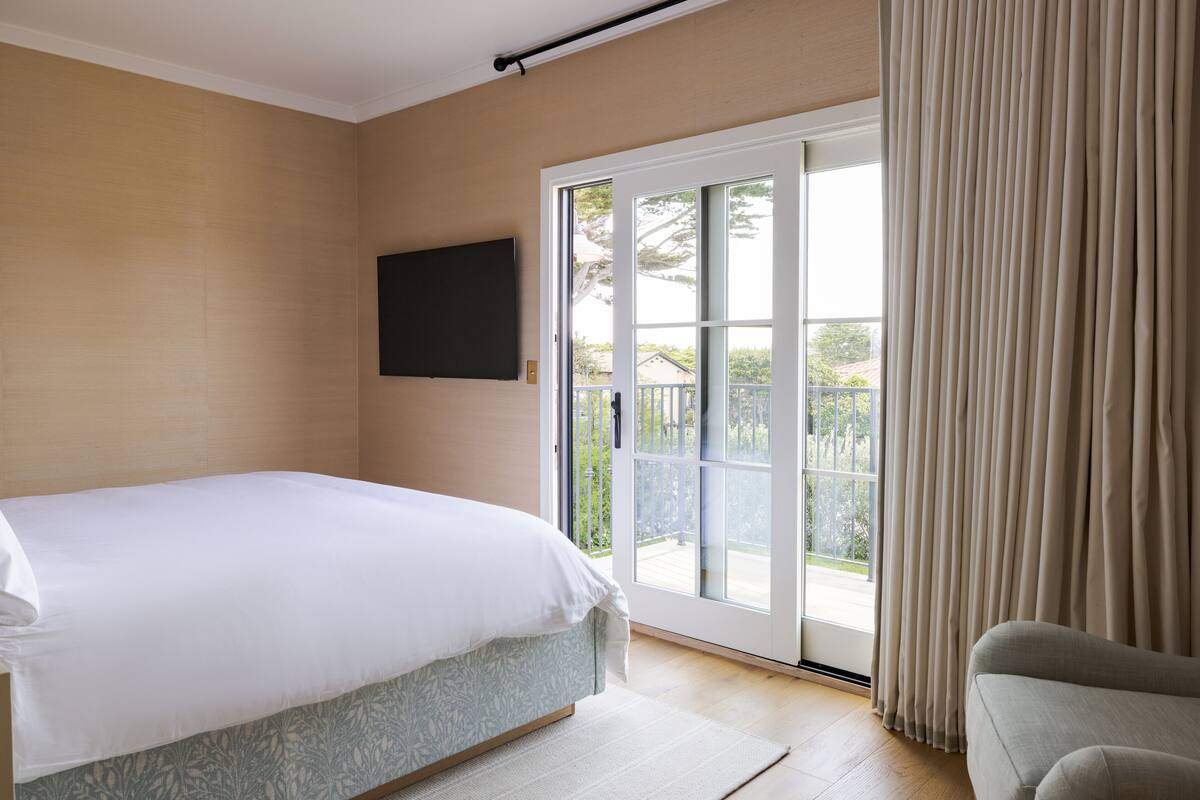 A bedroom with a bed, a TV mounted on the wall, and a sliding glass door leading to a balcony.