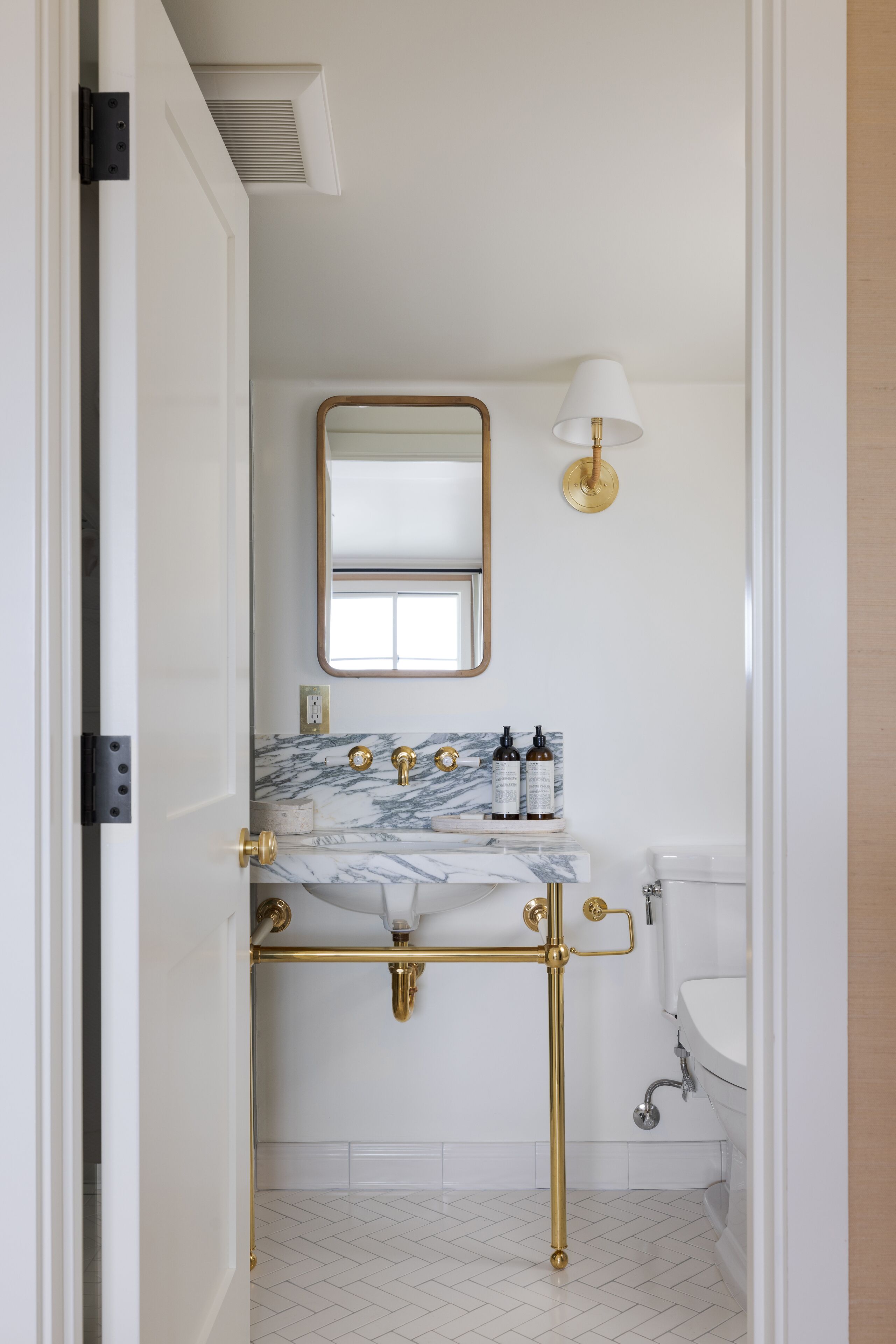 A bathroom with a marble sink, gold fixtures, a mirror, and a toilet.