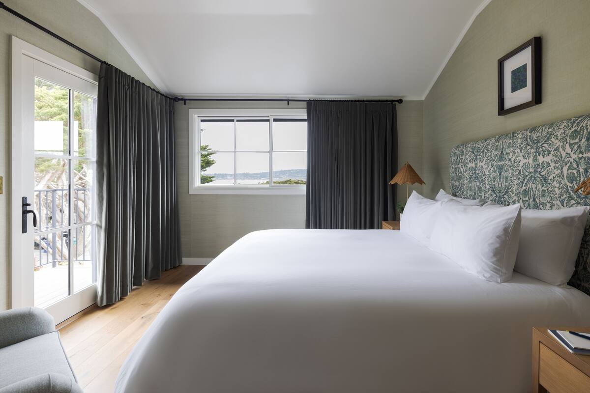 A hotel room with a large bed, a view of the outdoors through a window, and a balcony.