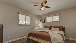 A bedroom with a bed, a ceiling fan, two windows with blinds, a bedside lamp, a bench, and a patterned rug. - **Newly Remodeled Home** 1 mile from Prescott Courthouse! (Prescott)