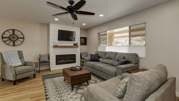 A modern living room with a fireplace, grey sofas, a ceiling fan, and a large window. - **Newly Remodeled Home** 1 mile from Prescott Courthouse! (Prescott)
