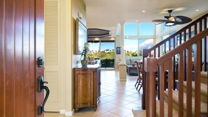 A spacious hallway with a wooden door, a wooden cabinet, and a staircase leading to a balcony with a view of greenery. - Mauna Lani Palm Villas H4 Corner Two-story Villa with Floor to Ceiling Views (Kamuela)