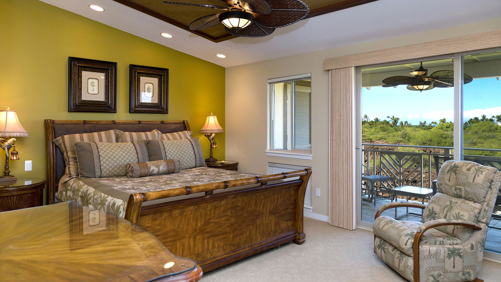 A bedroom with a large bed, two bedside lamps, and a view of a balcony with outdoor furniture.