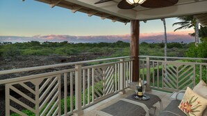 A covered outdoor seating area with a view of a volcanic landscape and a sunset. - Mauna Lani Palm Villas H4 Corner Two-story Villa with Floor to Ceiling Views (Kamuela)