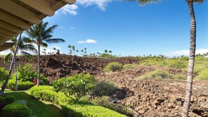 A volcanic landscape with a clear sky, palm trees, and a building with a sloped roof. - Mauna Lani Palm Villas H4 Corner Two-story Villa with Floor to Ceiling Views (Kamuela)