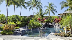 A resort pool area with lounge chairs, palm trees, and a waterfall feature. - Mauna Lani Palm Villas H4 Corner Two-story Villa with Floor to Ceiling Views (Kamuela)