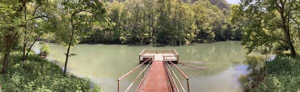 A wooden dock extending into a calm river surrounded by dense greenery.