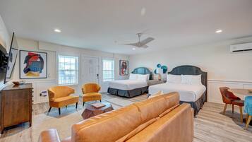A hotel room with a large bed, two bedside tables, a sofa, a chair, a desk, and a ceiling fan.