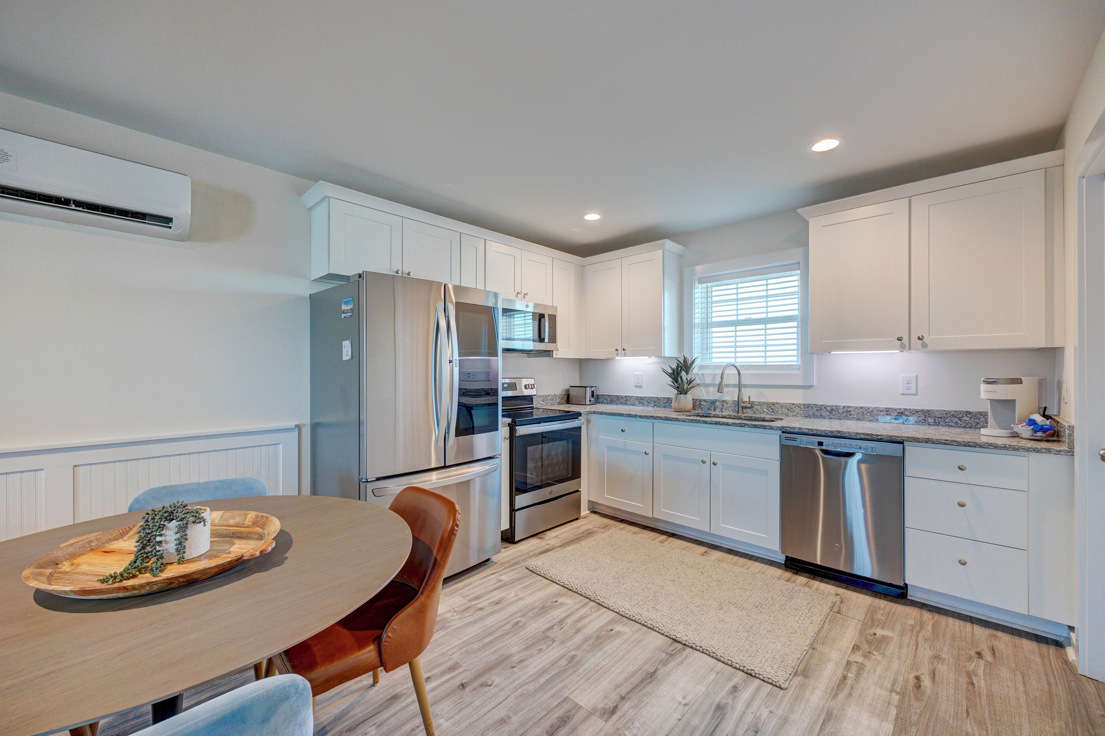A modern kitchen with white cabinets, stainless steel appliances, and a wooden dining table with chairs.