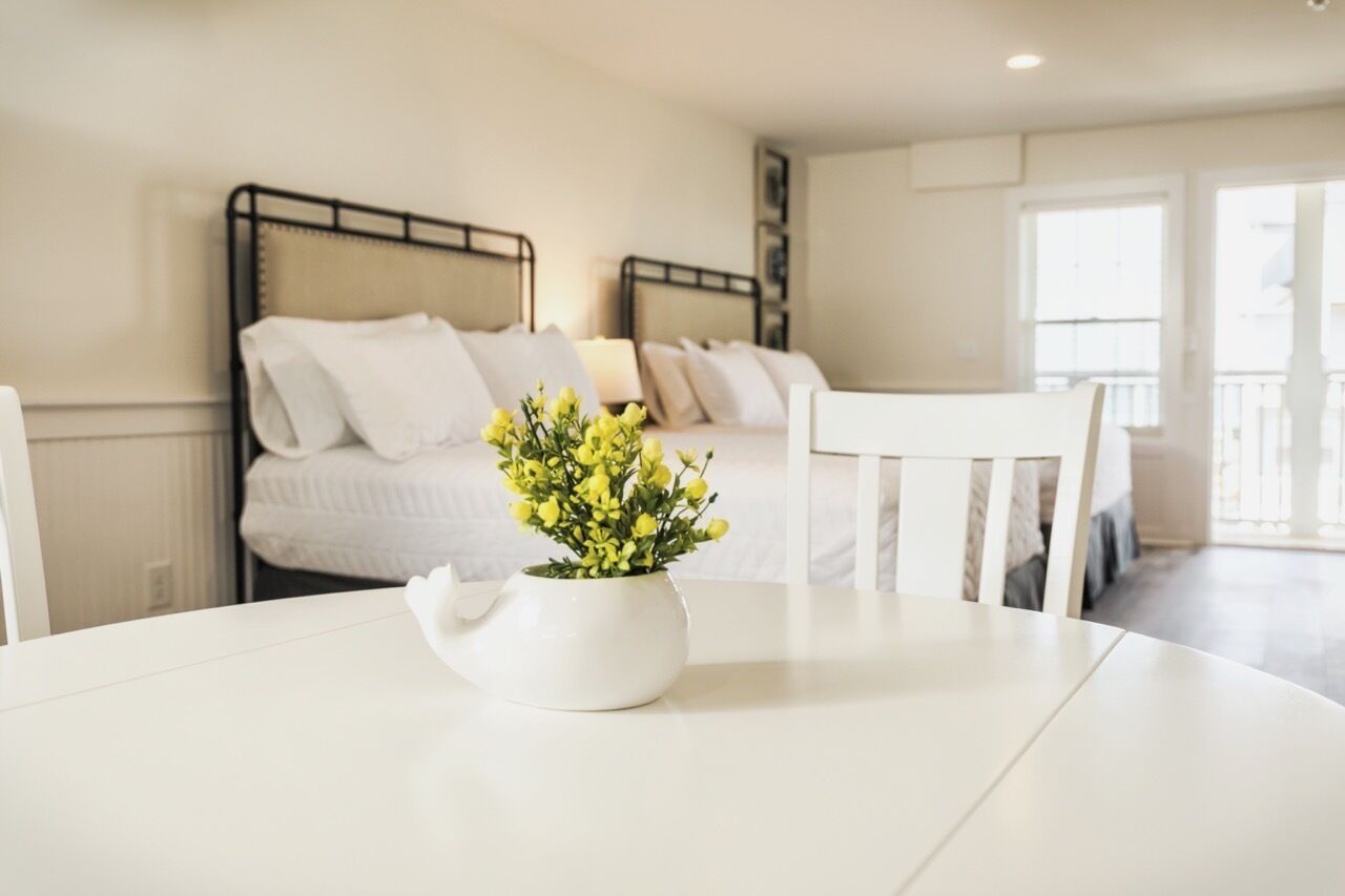 A bedroom with two beds, a white table with a vase of flowers, and a balcony with a railing.