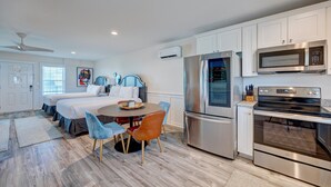 A modern kitchen with stainless steel appliances, a dining area with a round table and chairs, and a bedroom with a bed and a ceiling fan.