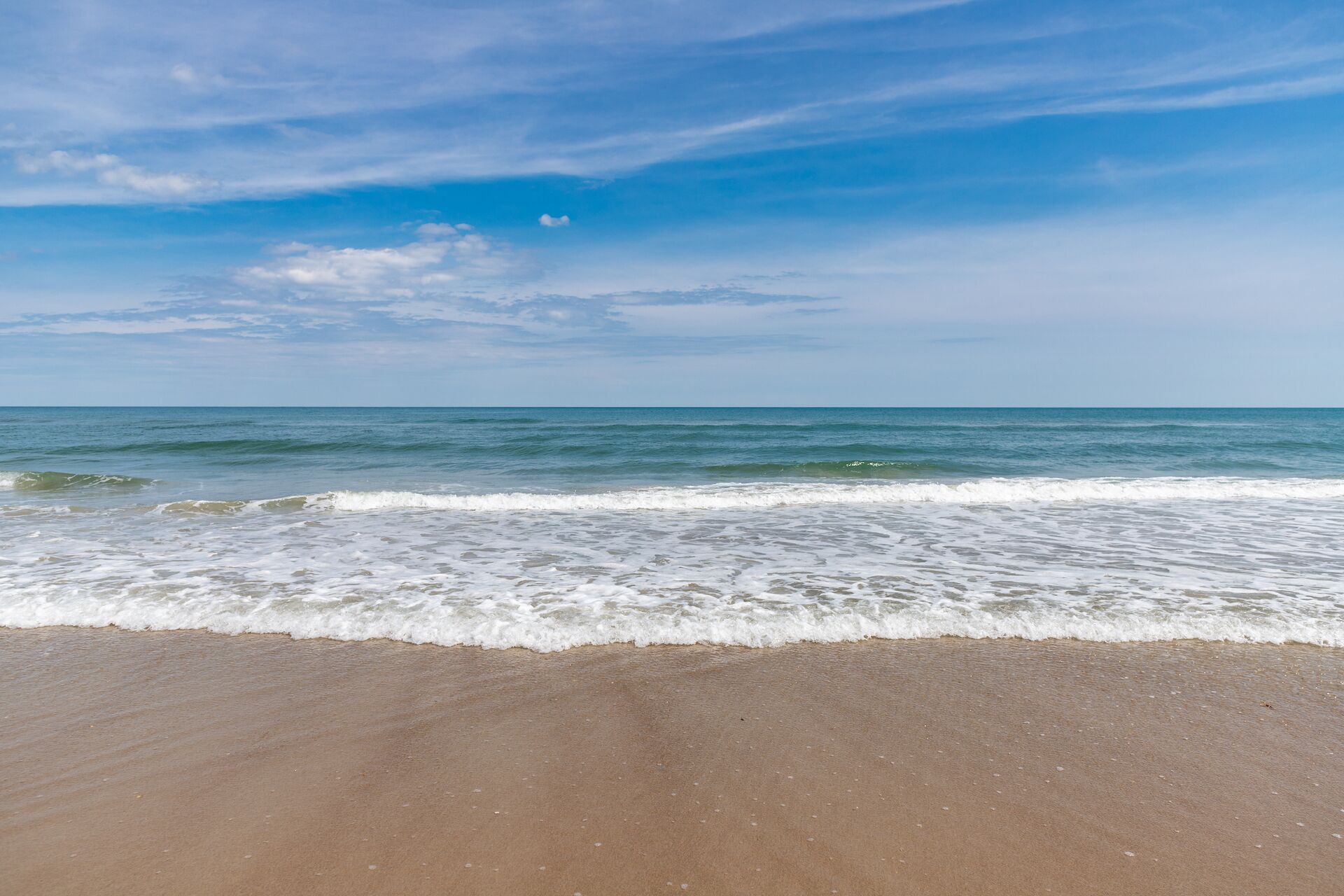 Une plage où les vagues se brisent près du rivage, sous un ciel dégagé.