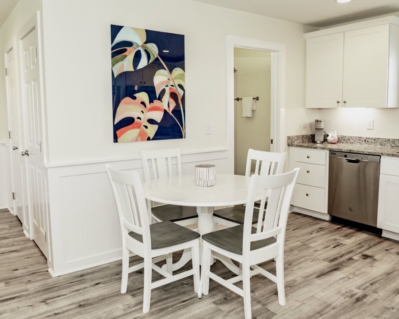 A modern kitchen with white cabinetry, a dining table with chairs, and a colorful abstract painting on the wall.