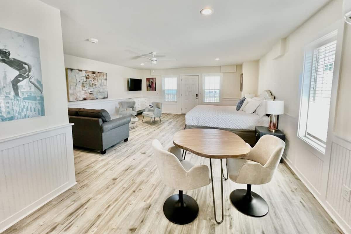A spacious room with a large bed, a dining table with chairs, a sofa, a TV, and artwork on the walls.