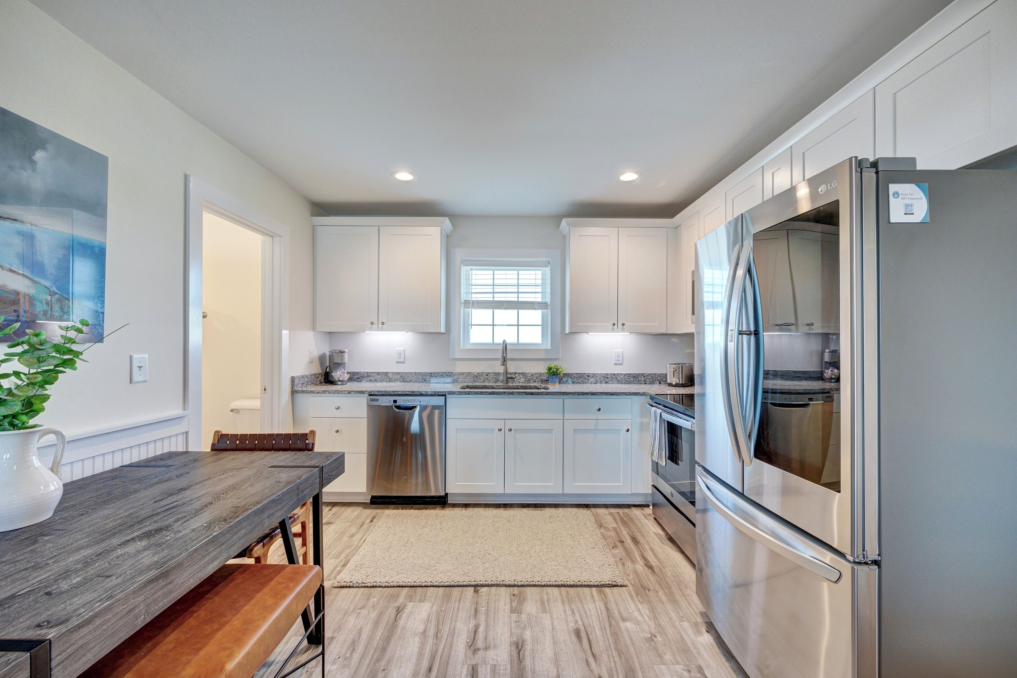 A modern kitchen with white cabinets, stainless steel appliances, and a wooden bench.