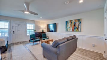 A living room with a gray sofa, teal chairs, a wooden coffee table, a TV mounted on the wall, and a large abstract painting.
