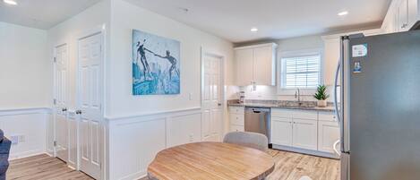 A modern kitchen with white cabinetry, a stainless steel refrigerator, and a dining area with a wooden table and chairs.