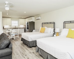 A hotel room with two beds, a kitchenette, a dining area, and a ceiling fan.