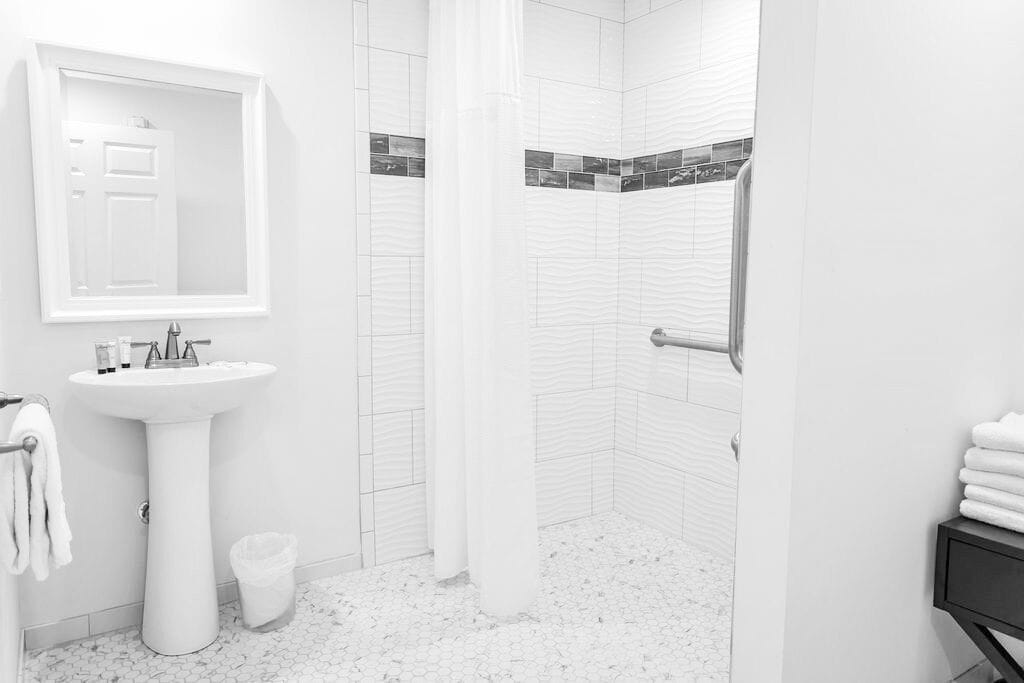 A modern bathroom with a pedestal sink, a mirror, a shower with a curtain, and a tiled floor.