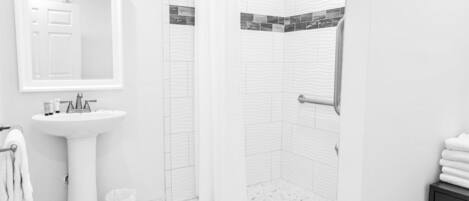 A modern bathroom with a pedestal sink, a mirror, a shower with a curtain, and a tiled floor.