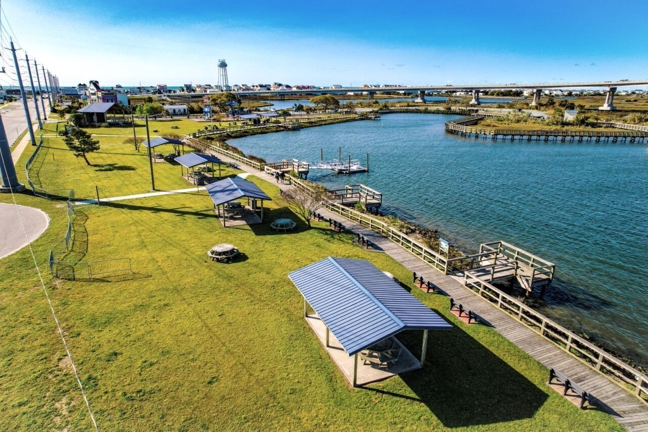 Eine Vogelperspektive auf einen Flussuferpark mit Spazierwegen, Picknickplätzen und einer Brücke im Hintergrund.