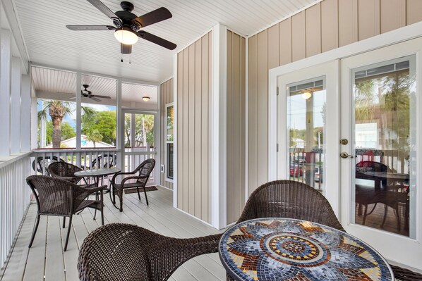 A covered porch with wicker furniture, a ceiling fan, and a glass door. - Parade Perfect, South Beach house (Tybee Island)