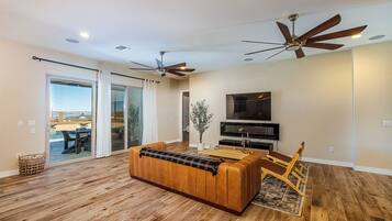 A spacious living room with a wooden floor, a leather sofa, a wooden coffee table, and two ceiling fans.