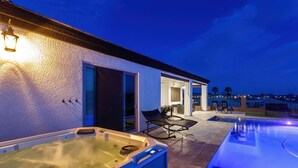 Een modern zwembadgedeelte buiten, met een jacuzzi, ligbedden en een terras met uitzicht op de stadshemel bij zonsondergang.
