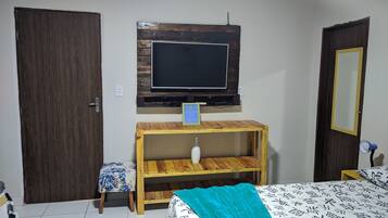 Un dormitorio con una cama de madera, un televisor montado en un estante de madera, un taburete pequeño y un espejo en la pared.
