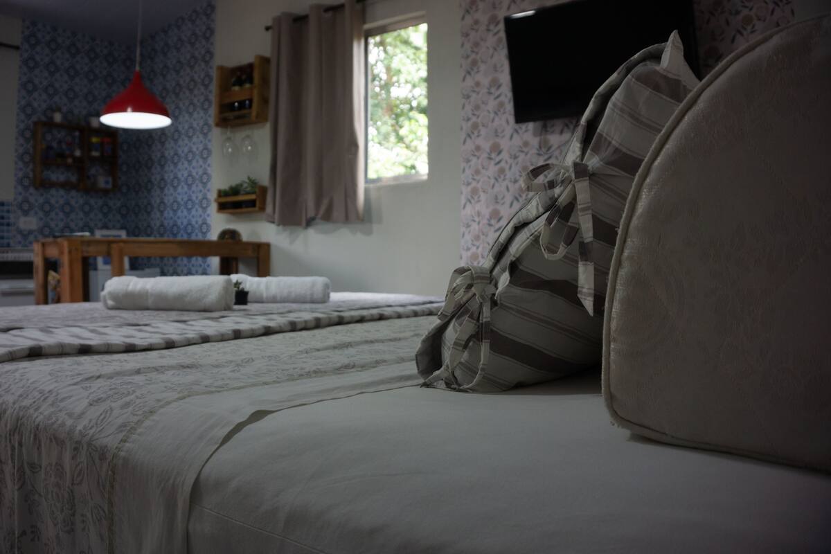 A bedroom with a bed, a red pendant light, a window, and a television on the wall.