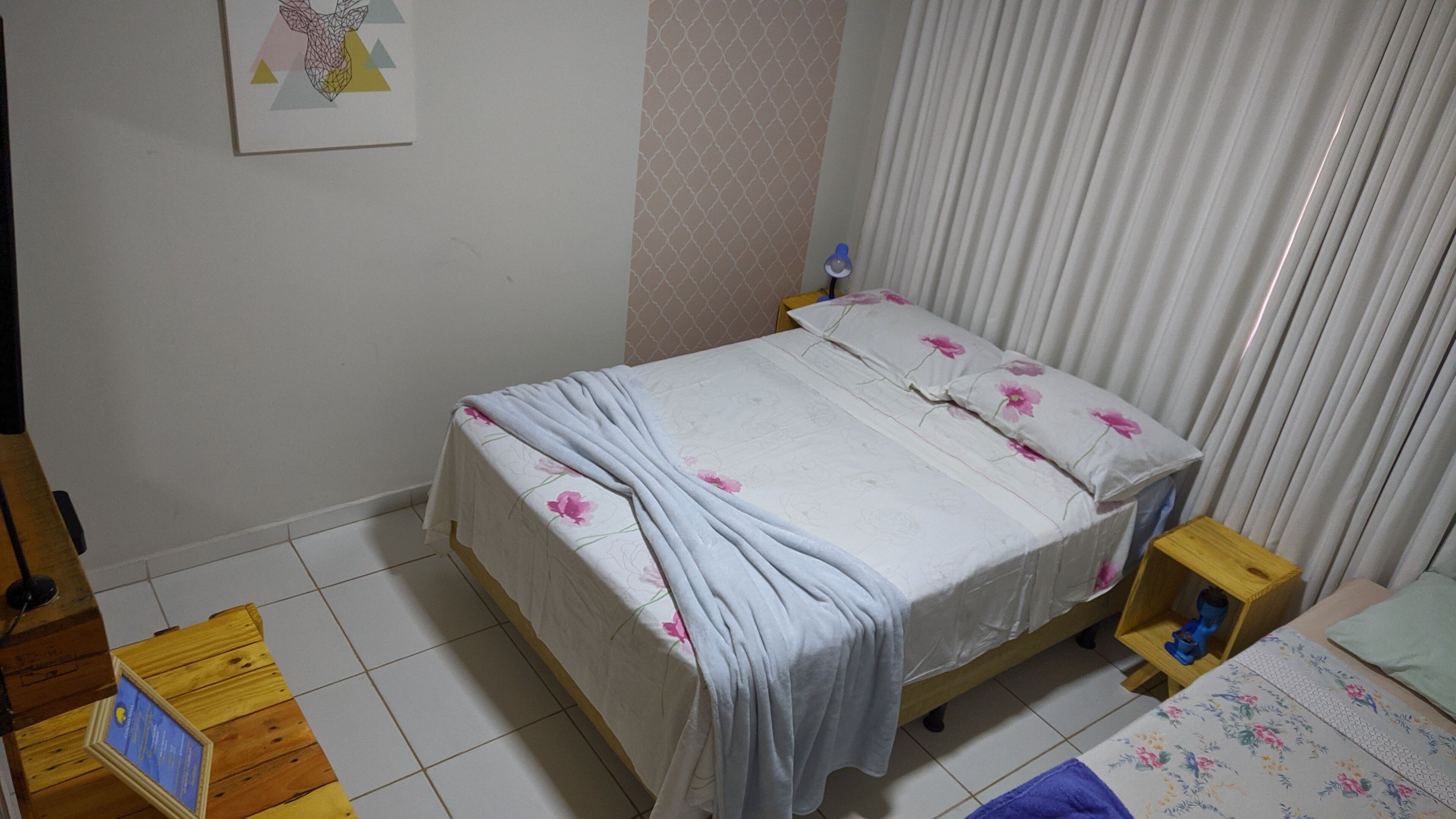 A bedroom with a bed, a nightstand, a wooden table, and a small shelf.