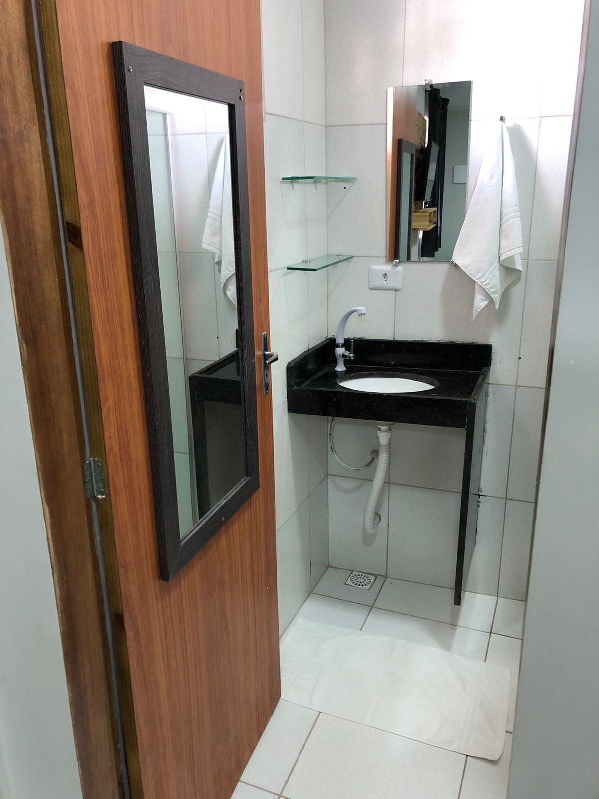 A bathroom with a wooden door, a black sink, a mirror, and a glass shelf.