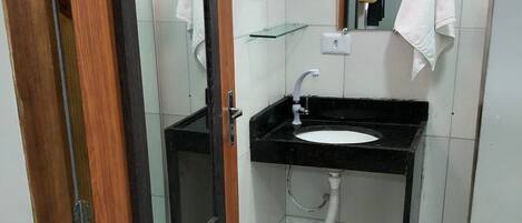 A bathroom with a wooden door, a black sink, a mirror, and a glass shelf.