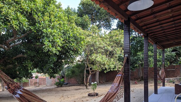 Una hamaca bajo una pérgola de madera en un jardín con árboles y un muro de ladrillo.