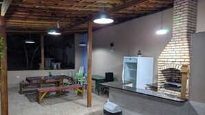Un patio interior con chimenea de ladrillo, mesas y sillas de madera, y un cubo de basura.