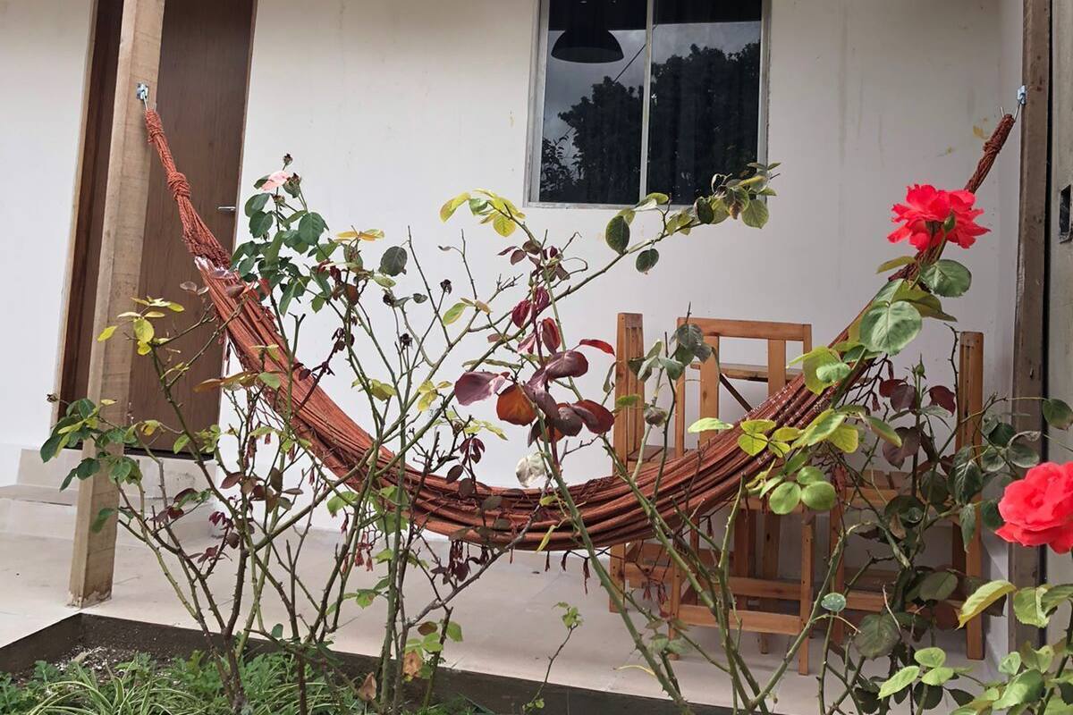 A hammock tied between two wooden posts in front of a building with a tiled roof and a window.