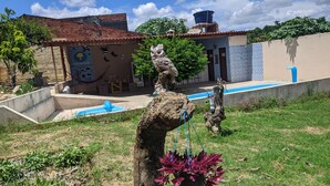 Un patio con piscina, una escultura de árbol rústica y un edificio con fachada de azulejos.