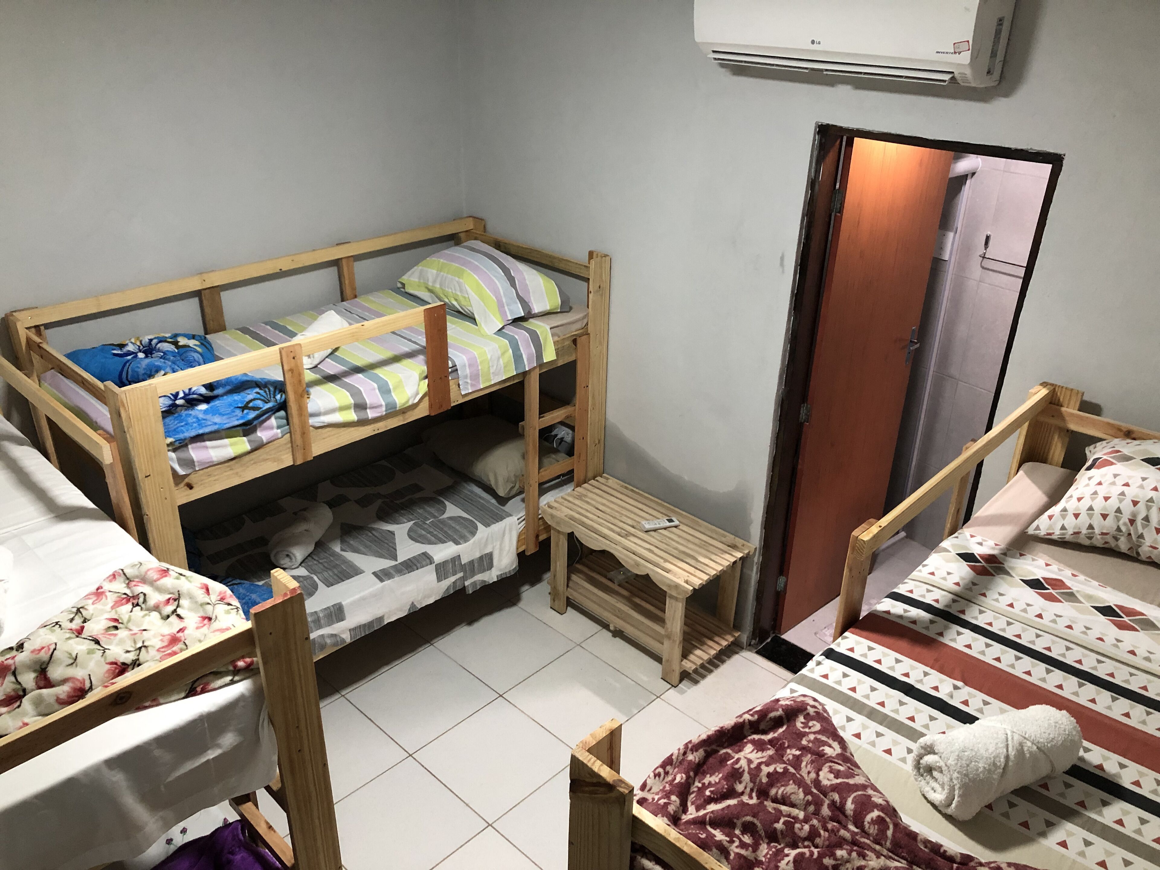 Habitación tipo dormitorio con literas, una pequeña mesa de madera, una puerta y un equipo de aire acondicionado en la pared.