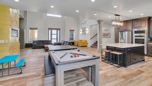 Un amplio salón con mesa de billar, sofá y cocina equipada con electrodomésticos modernos.