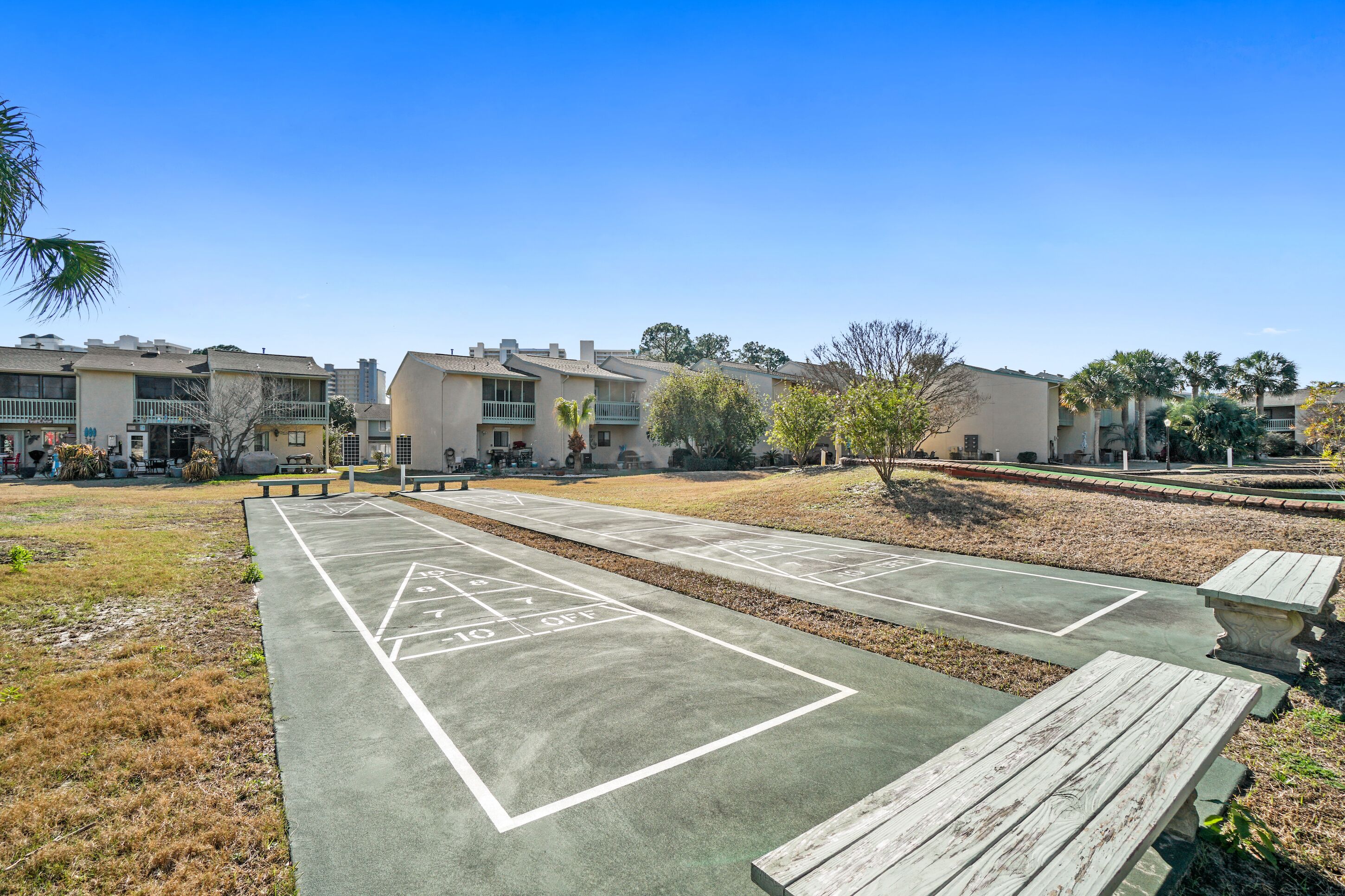 A shuffleboard court with wooden benches, surrounded by residential buildings and trees.
