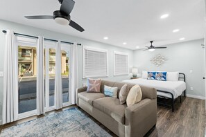 A bedroom with a bed, a sofa, a ceiling fan, and a view through a sliding door.