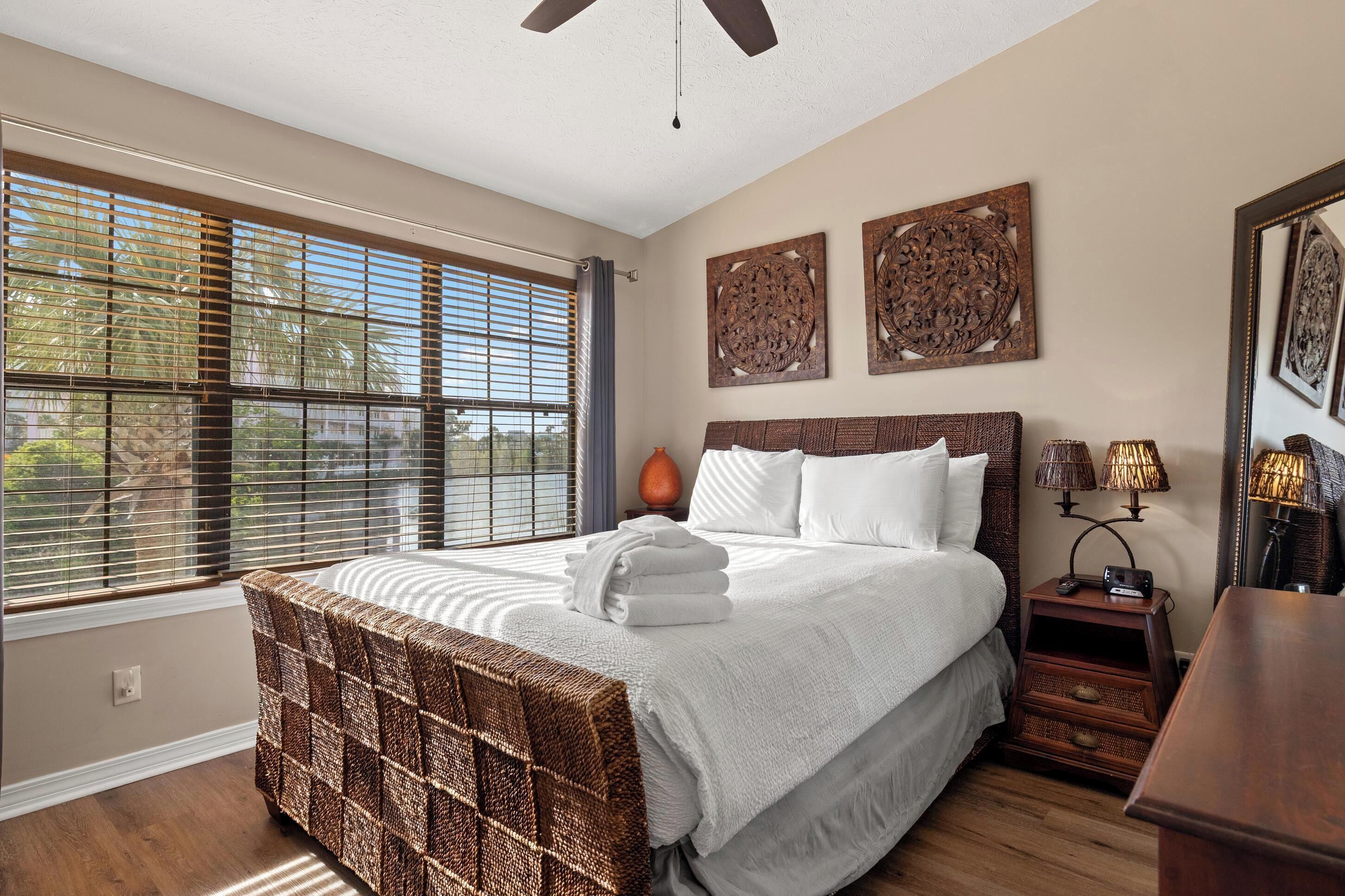 A bedroom with a large bed, a bedside table with lamps, and a window with blinds.