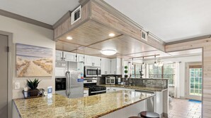 Uma cozinha com bancada de granito, armários brancos, eletrodomésticos de aço inoxidável e uma grande ilha com banquetas.